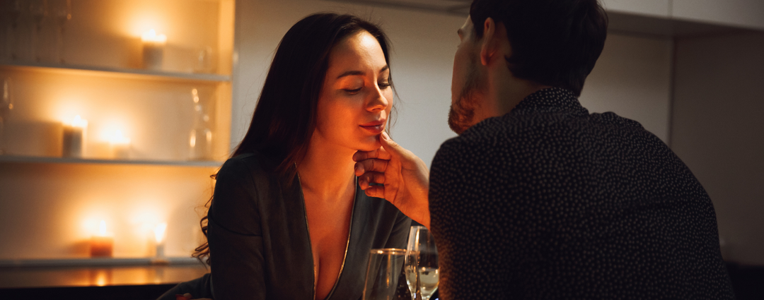 A couple enjoying a romantic candlelit dinner at home, with the man gently touching the woman's chin.