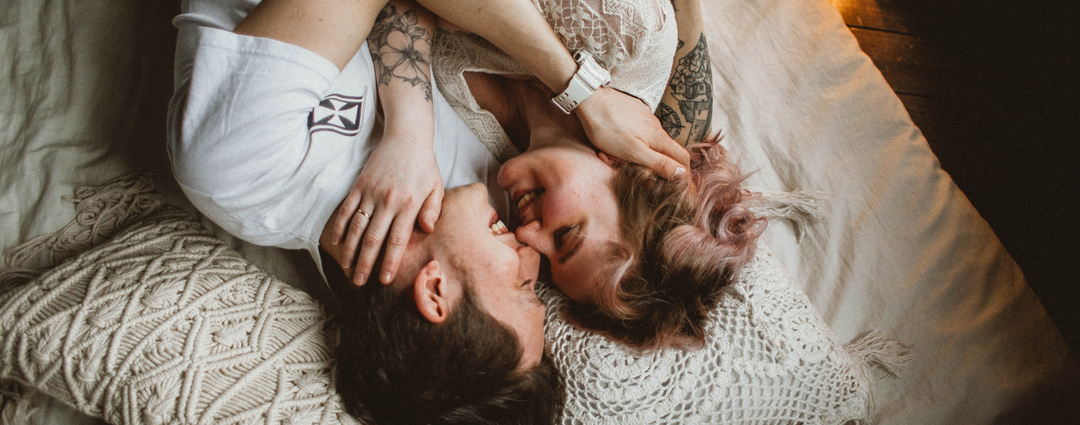 Couple cuddling and smiling together on a bed, symbolizing love and intimacy.